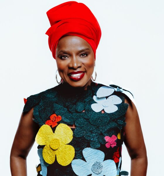 Studio portrait of Benin-born singer Angélique Kidjo smiling in a floral appliqué sleeveless top and a vibrant red headwrap.