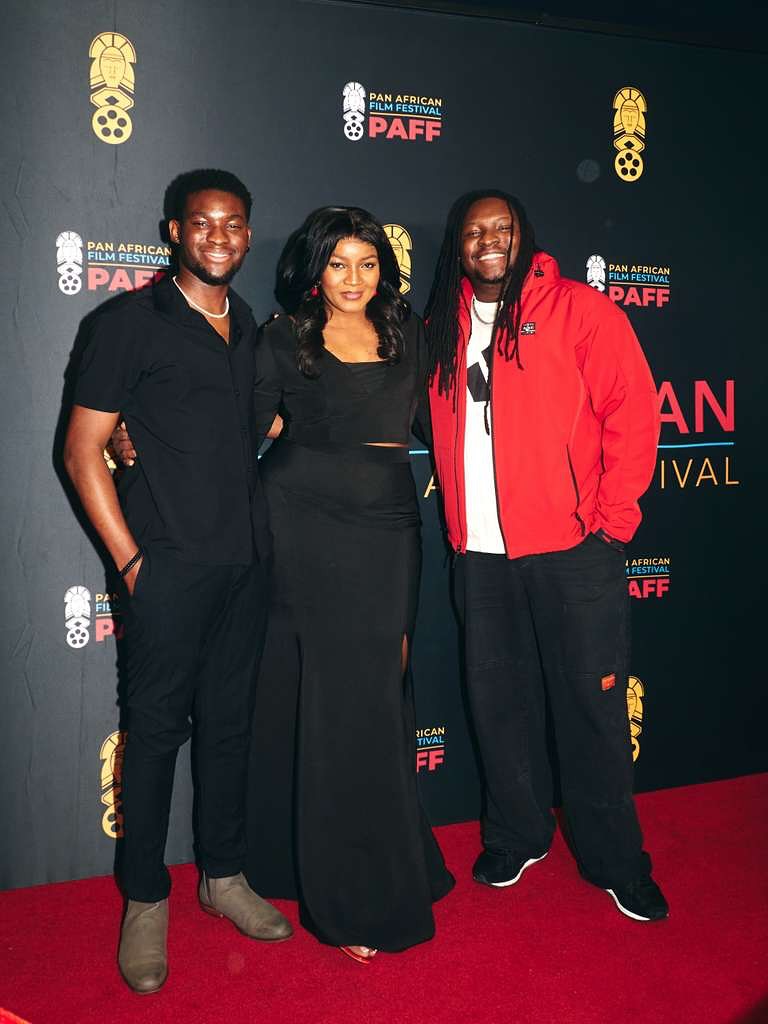 Omotola Jalade-Ekeinde posing on the red carpet flanked by her two sons, Matthew and Michael Ekeinde, at the Pan African Film Festival backdrop.