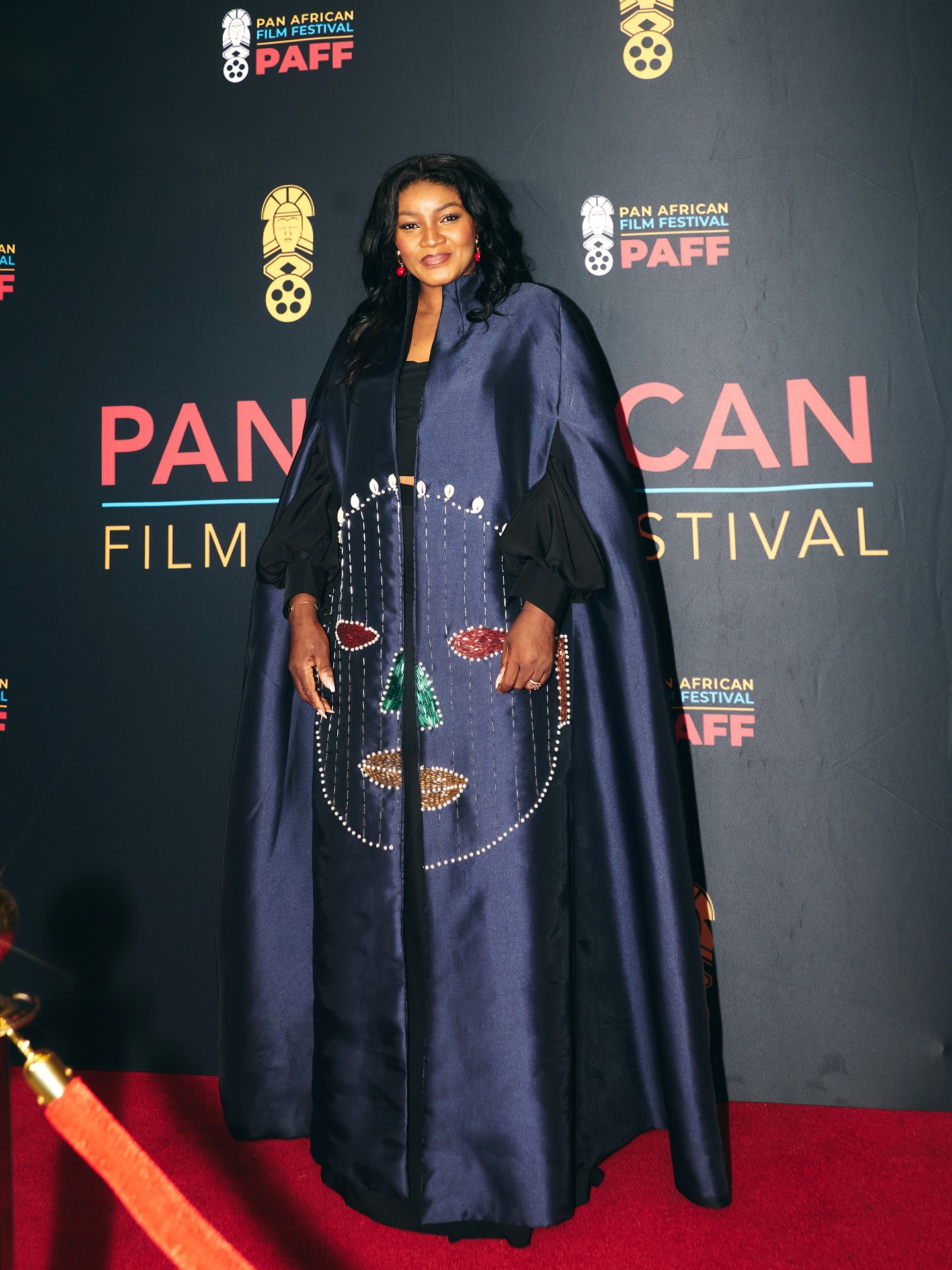 Omotola Jalade-Ekeinde wearing a floor-length navy blue cape coat with metallic face embellishments at the 34th Pan African Film Festival carpet.