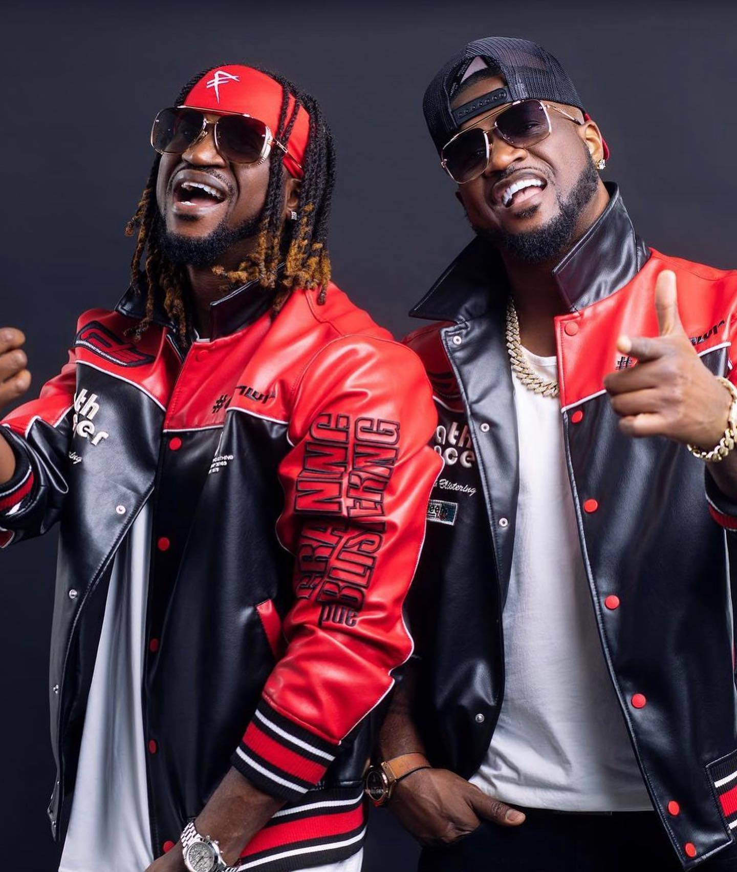 Peter and Paul Okoye of P-Square posing in matching red and black leather biker jackets, sunglasses, and gold chains.
