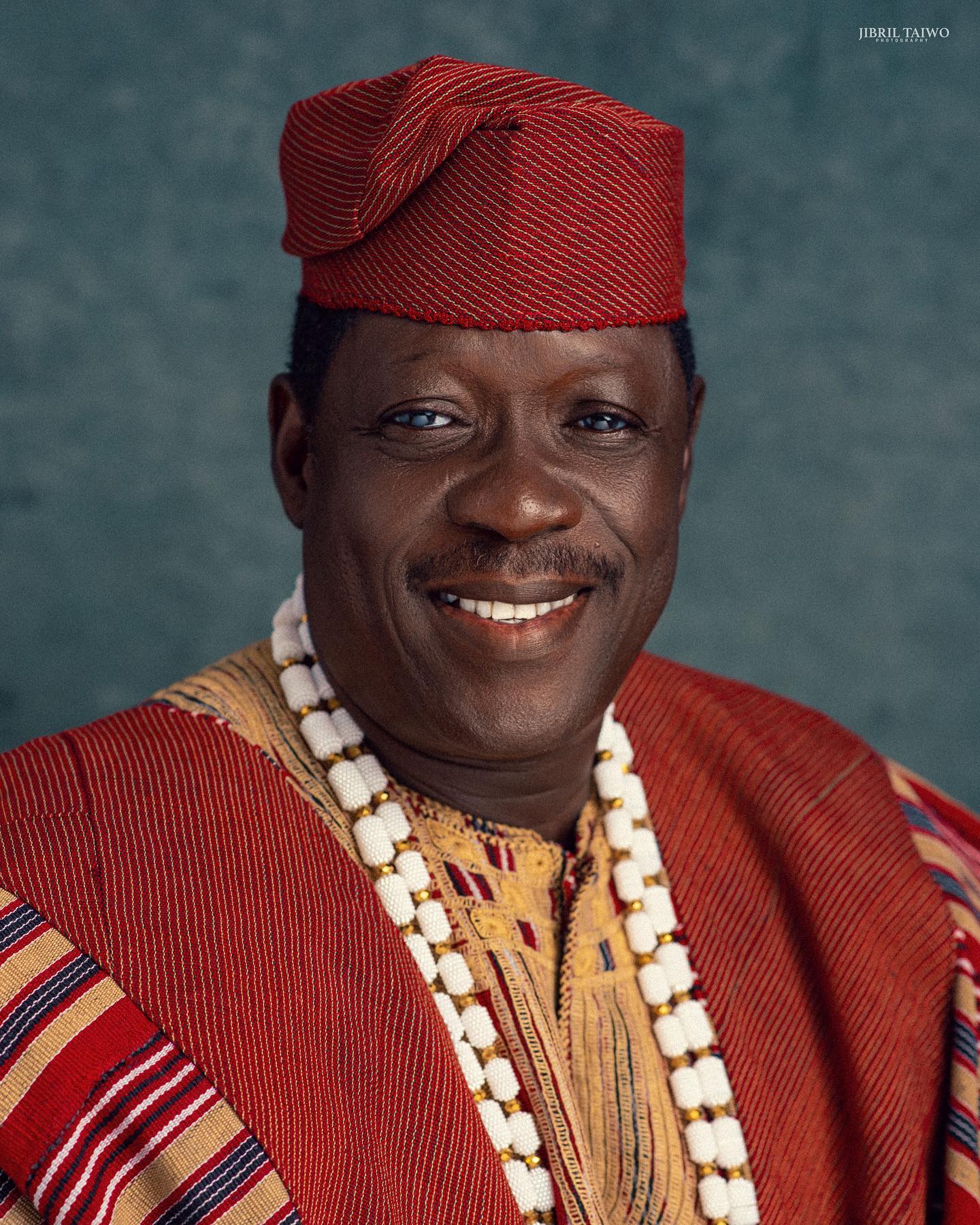 Nollywood icon Taiwo Hassan Ogogo smiling in a traditional red Aso-Oke Fila cap and white coral beads.