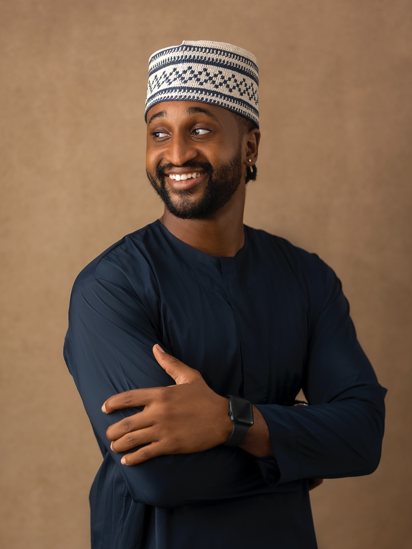 Chimsom Chuka smiling in a dark navy blue kaftan and a patterned embroidered cap.