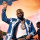 Afrobeats artist Davido performing live on stage at Coachella 2026 with one hand raised, wearing a denim jacket and diamond chain.
