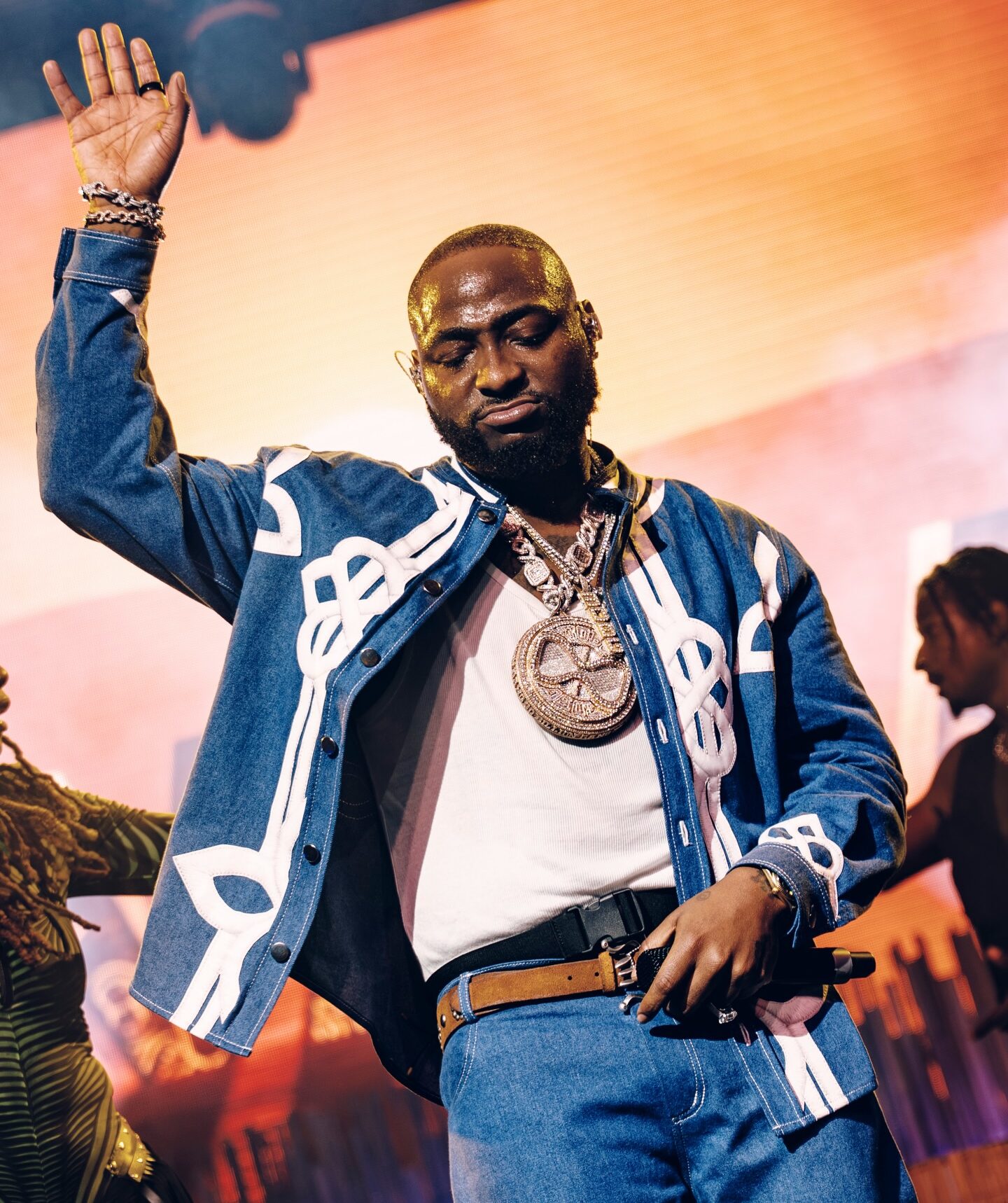 Afrobeats artist Davido performing live on stage at Coachella 2026 with one hand raised, wearing a denim jacket and diamond chain.