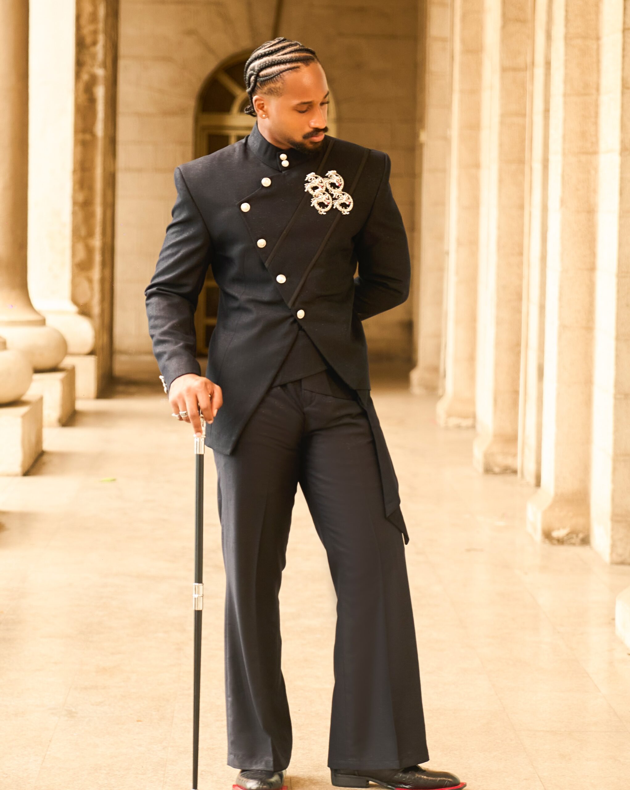 BBNaija housemate Chimsom Chuka posing in a dark asymmetrical military-inspired suit with white crest buttons, cornrow braids, and a walking cane at AMVCA 2026.