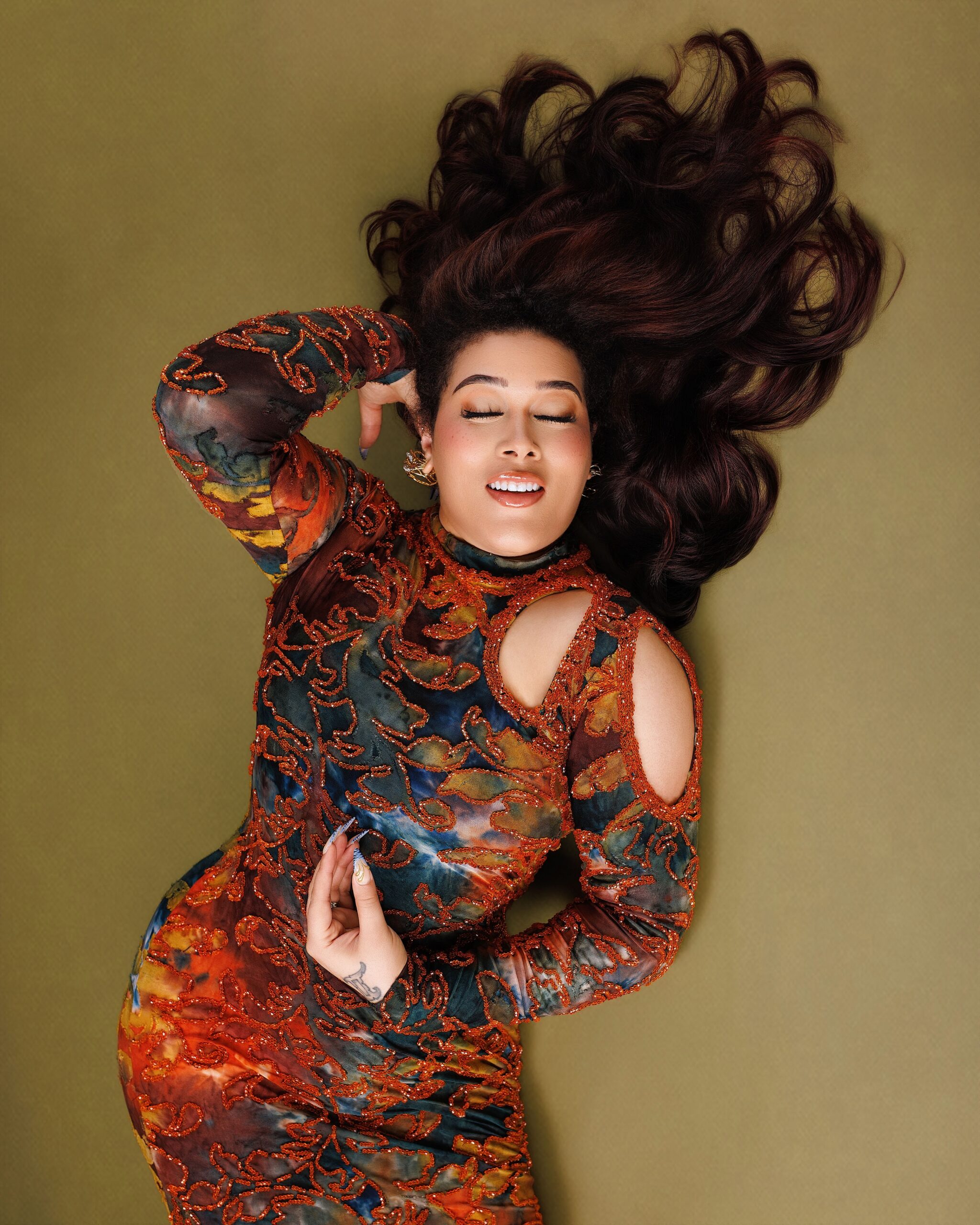 Adunni Ade lying down in an orange and teal patterned cut-out gown with her hair fanned out behind her.