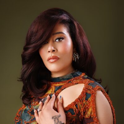 Adunni Ade wearing an orange-embellished patterned outfit with auburn styled hair.