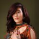 Adunni Ade wearing an orange-embellished patterned outfit with auburn styled hair.