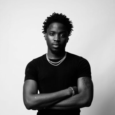 Nigerian singer Kunmie wearing a black t-shirt and silver chains in a monochrome portrait shot.