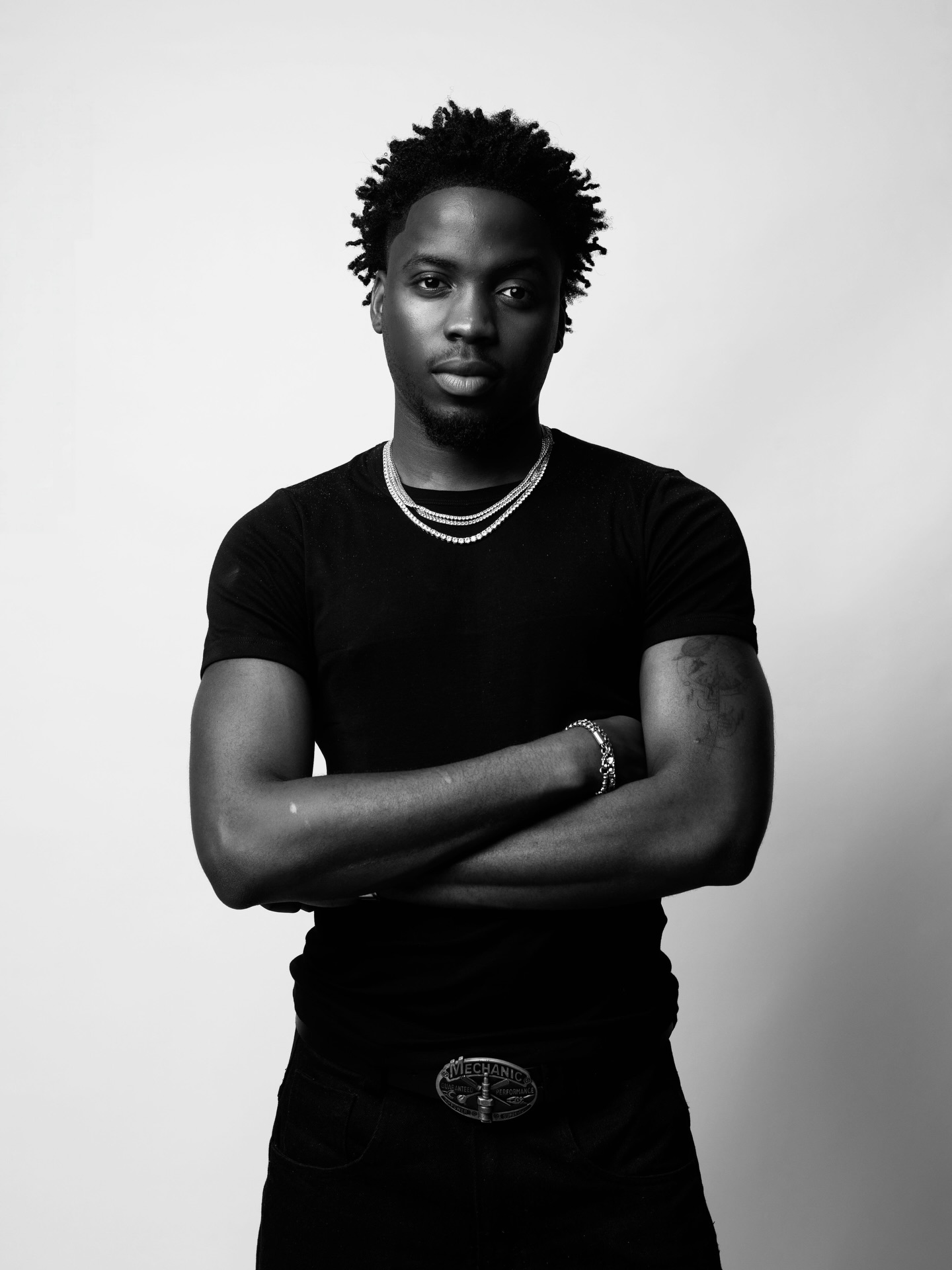 Nigerian singer Kunmie wearing a black t-shirt and silver chains in a monochrome portrait shot.