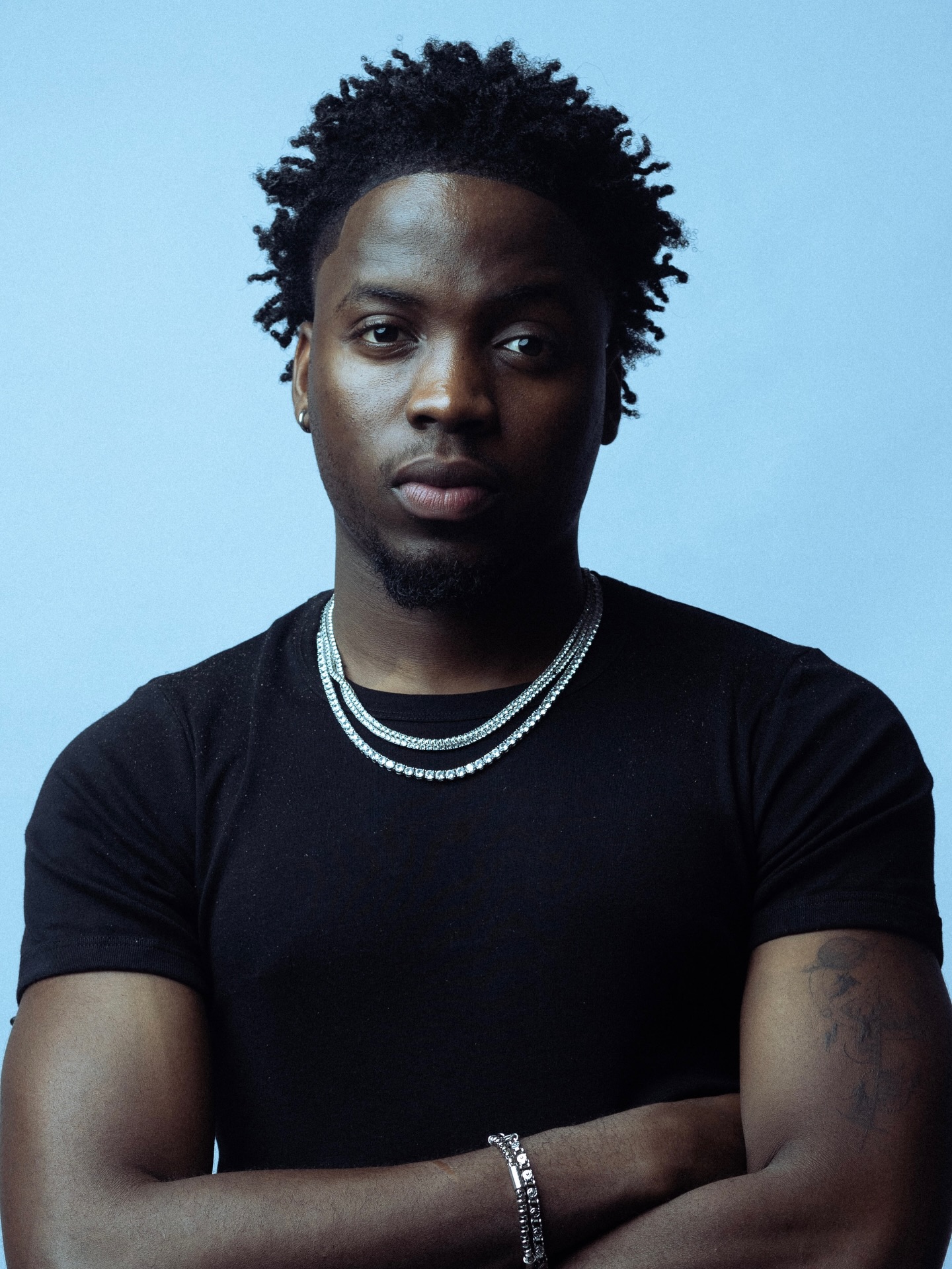 Nigerian R&B singer Kunmie wearing a black t-shirt and silver chain necklaces