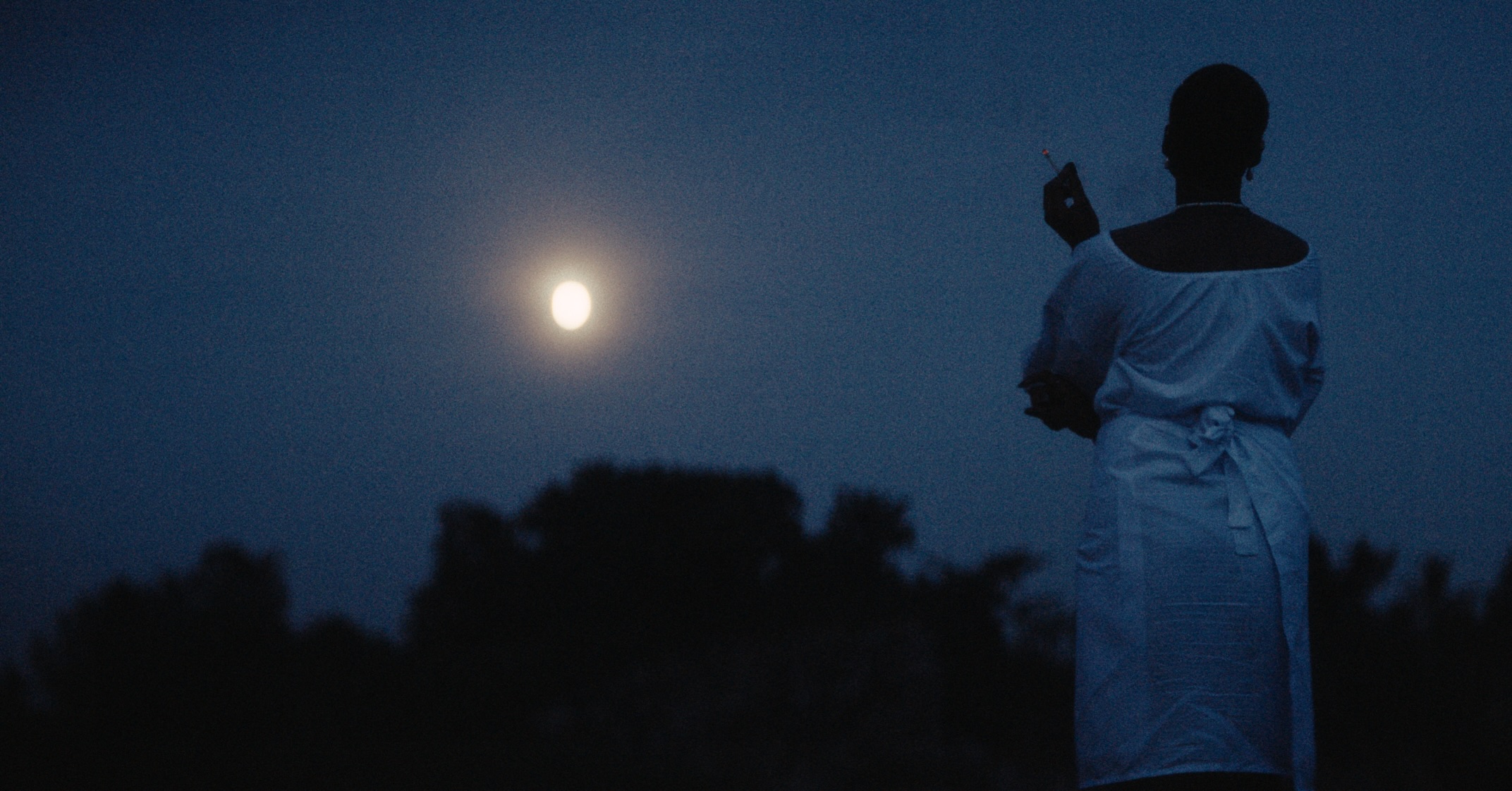 Tosin Adeyemi outdoors at night under a full moon in a scene from Damilola Orimogunje’s movie Dear Ajayi.
