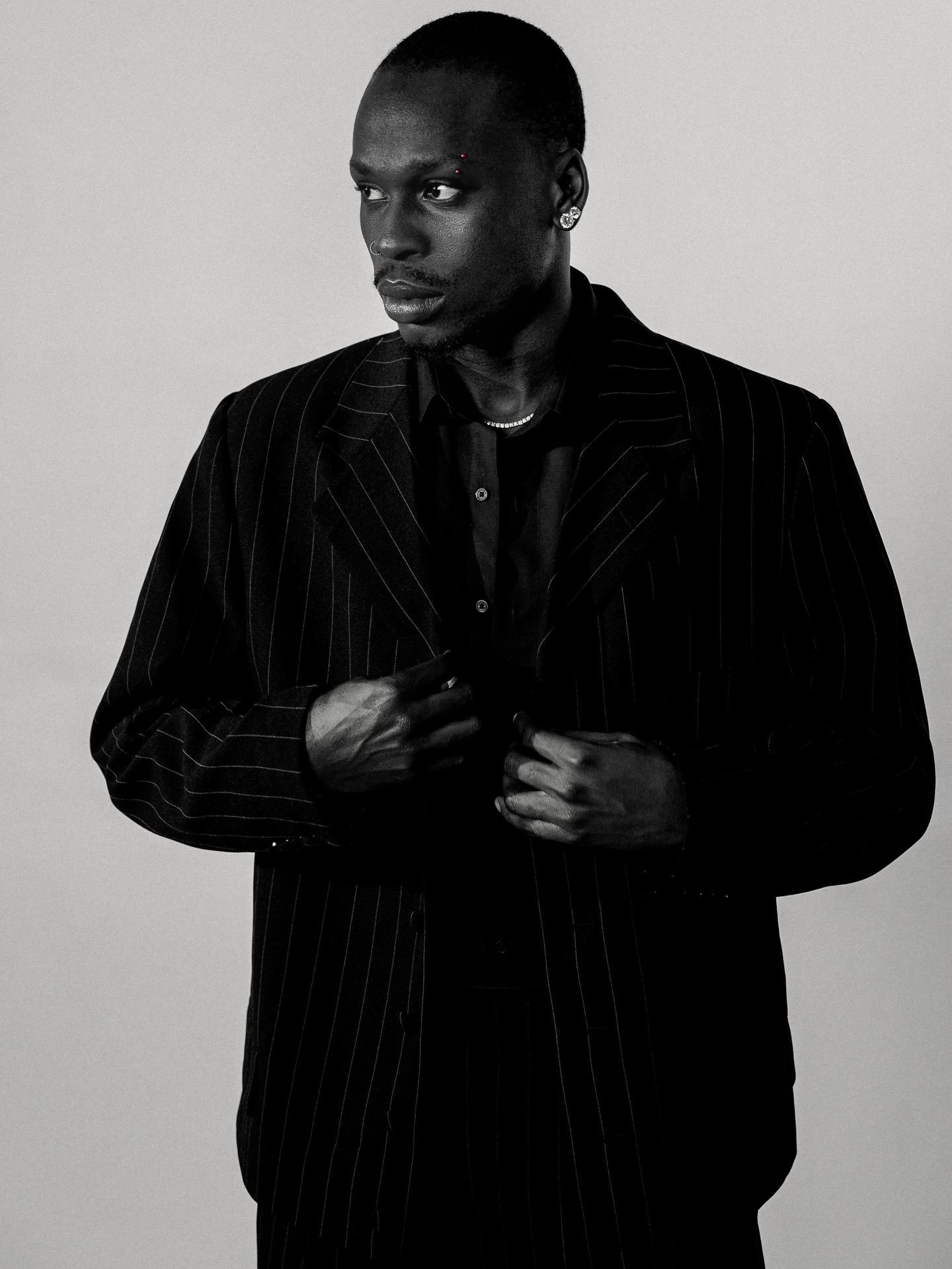 Fireboy DML posing in an unbuttoned black shirt and pinstripe suit jacket with silver tennis chains in promotional photos for his CLAAT release.