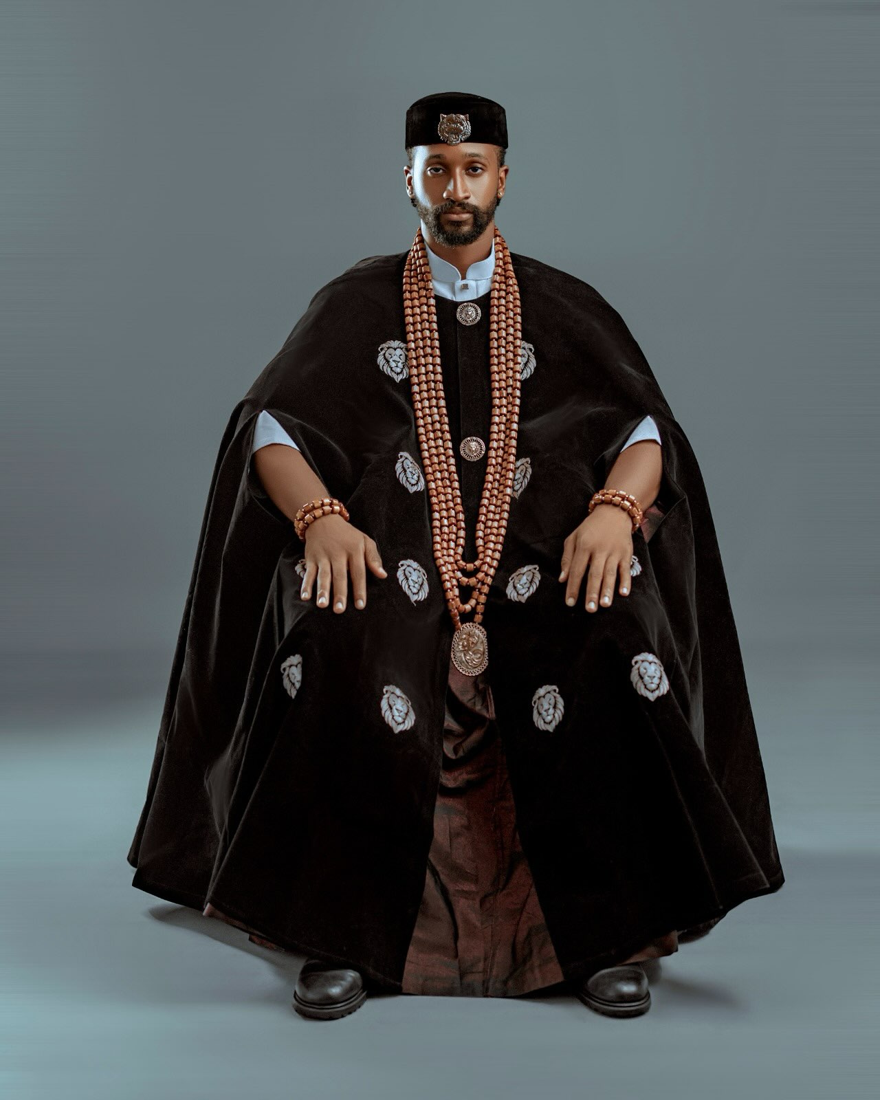 Chimsom Chuka seated in a regal black velvet cape outfit with lion crests and coral beads for the BBNaija Season 11 launch.