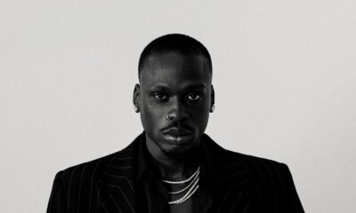 Black and white portrait of Nigerian Afrobeats artist Fireboy DML wearing a dark pinstripe suit jacket and layered silver chains ahead of his CLAAT single release.