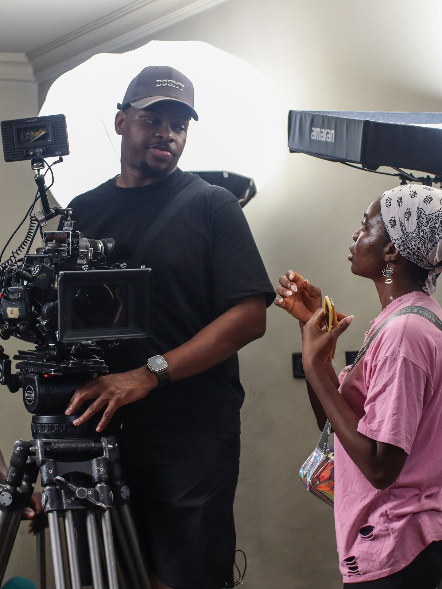 Director Uzoamaka Power wearing a patterned bandana reviewing camera framing with the cinematographer on the production set of Siraam.