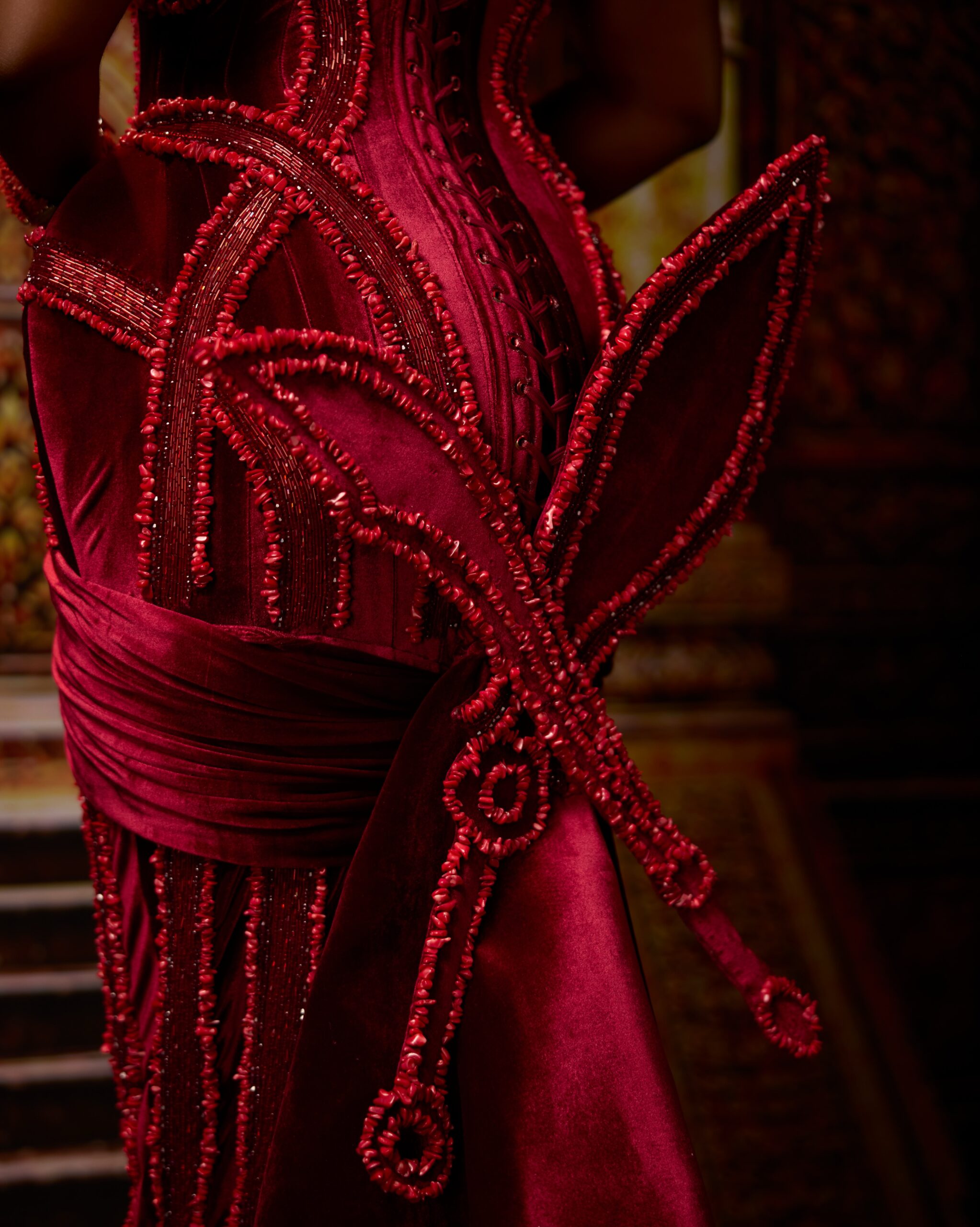 Back view of Jarvis's crimson velvet Edo traditional gown by Veekee James featuring corset lacing and structural Ada and Eben sword fins lined with coral beads.