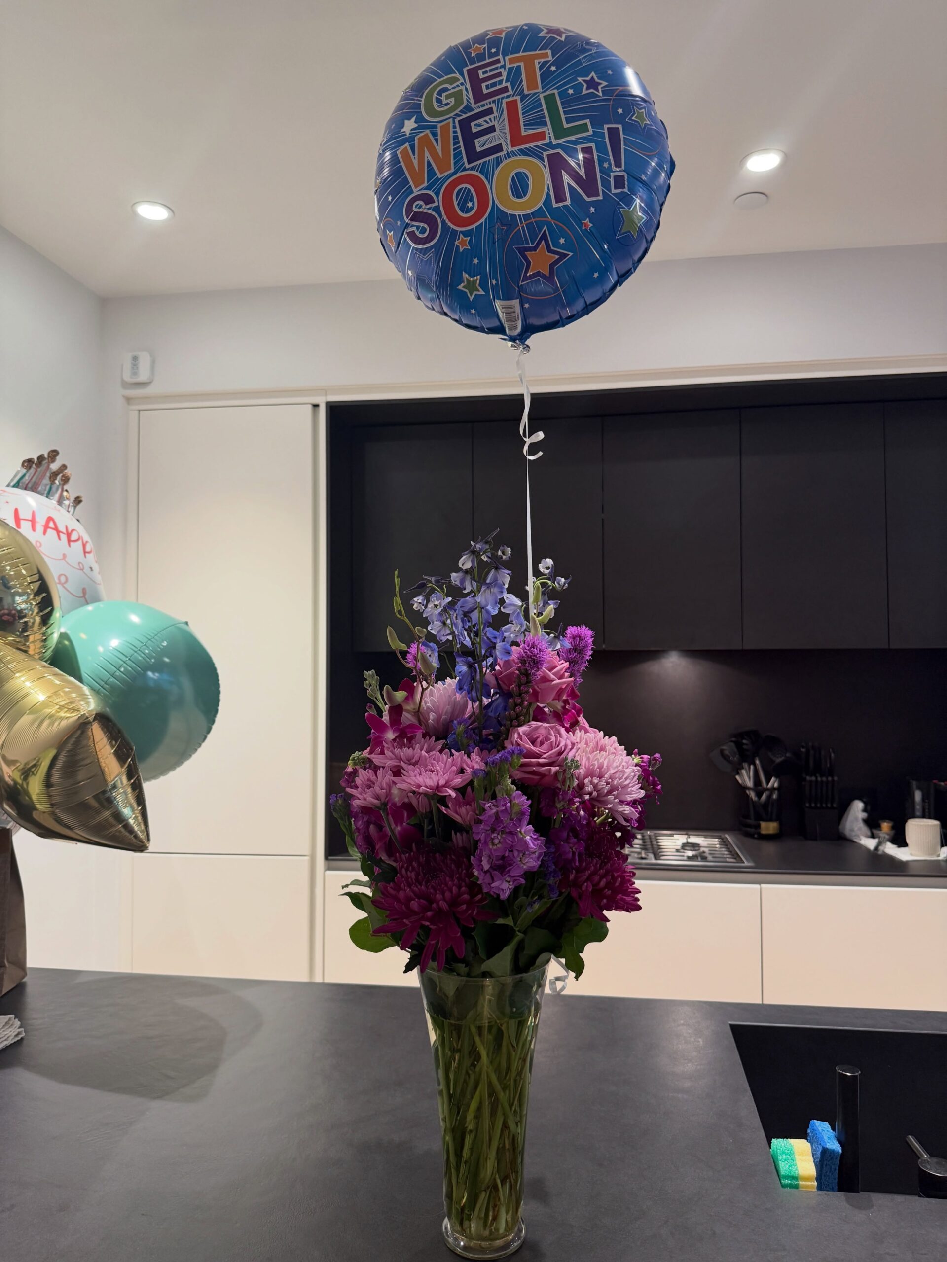 Purple and pink floral arrangement with a Get Well Soon balloon sent to Ayra Starr following major surgery recovery.