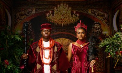 Peller and Jarvis posing in matching burgundy velvet traditional Edo wedding attire with coral beads and black ceremonial staff.