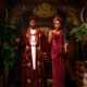 Peller and Jarvis posing in matching burgundy velvet traditional Edo wedding attire with coral beads and black ceremonial staff.