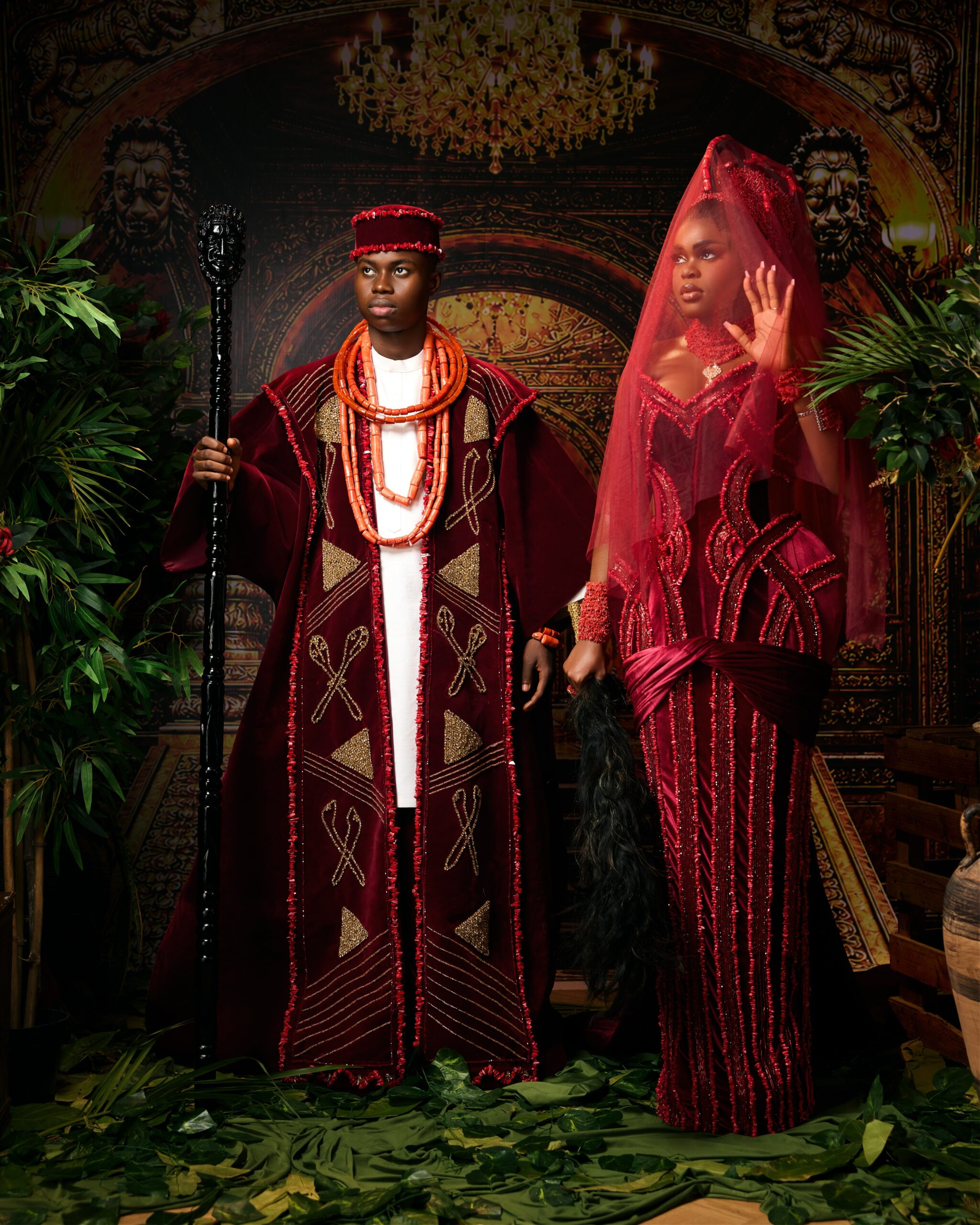 Peller holding a carved staff alongside Jarvis wearing a sheer red veil over her Okuku crown in traditional Edo wedding attire.