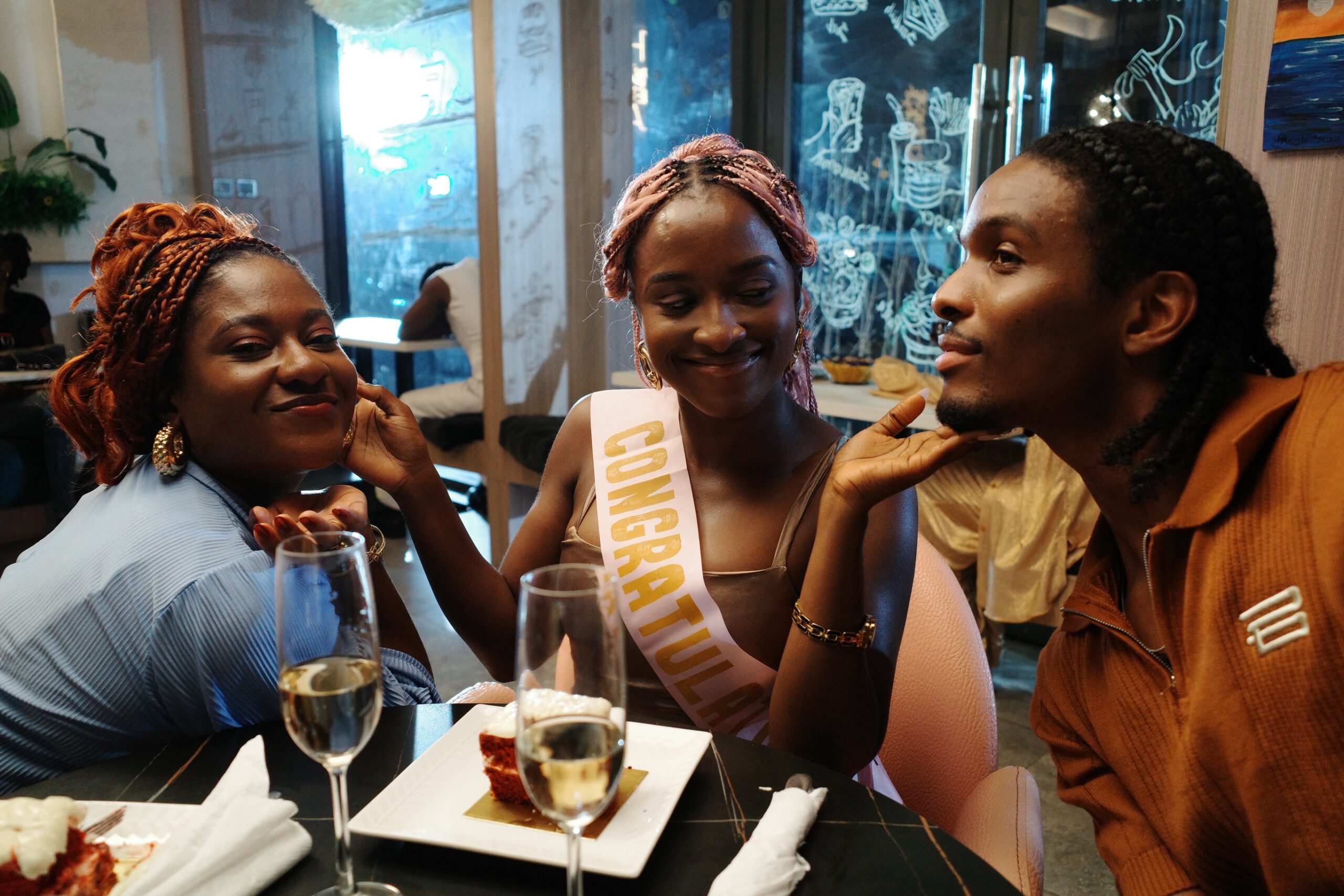 Genoveva Umeh wearing a congratulations sash alongside Natse Jemide at a restaurant table scene in the short film Siraam.