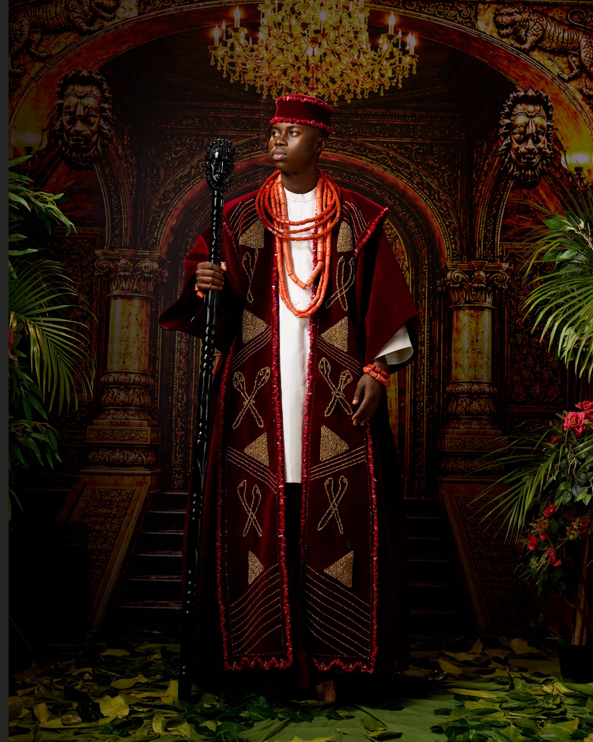 Peller wearing a deep burgundy velvet ceremonial robe by Amy Aghomi with coral neck beads, matching cap, and a carved wooden staff for his Edo traditional wedding.