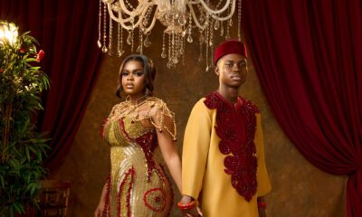 Peller and Jarvis holding hands in matching gold and burgundy custom traditional wedding outfits.
