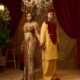 Peller and Jarvis holding hands in matching gold and burgundy custom traditional wedding outfits.
