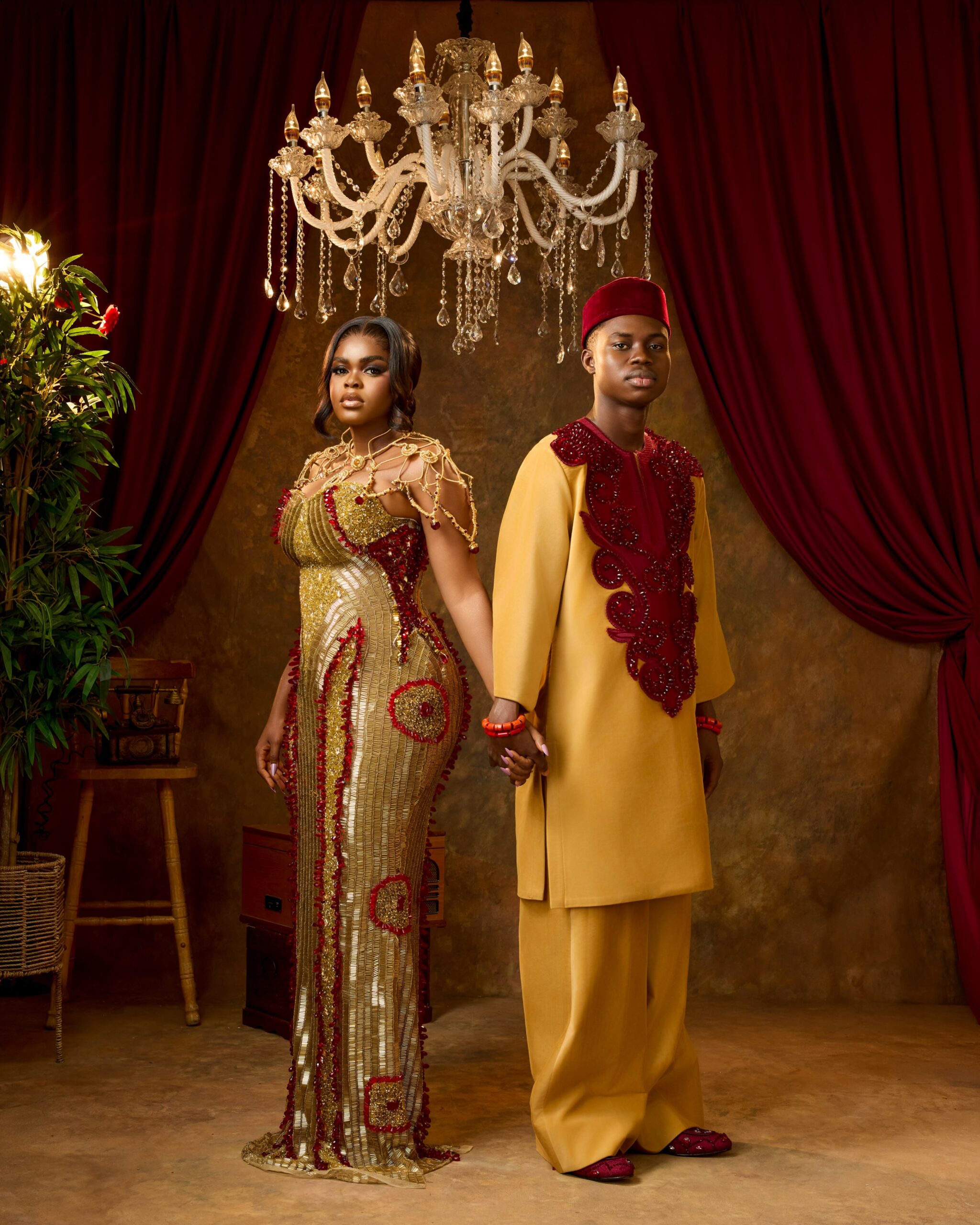 Peller and Jarvis holding hands in matching gold and burgundy custom traditional wedding outfits.
