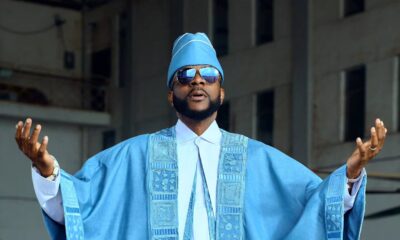 Ebuka Obi-Uchendu posing with arms outstretched displaying the wide wingspan of a sky-blue denim Agbada and white Buba tunic.