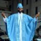 Ebuka Obi-Uchendu posing with arms outstretched displaying the wide wingspan of a sky-blue denim Agbada and white Buba tunic.