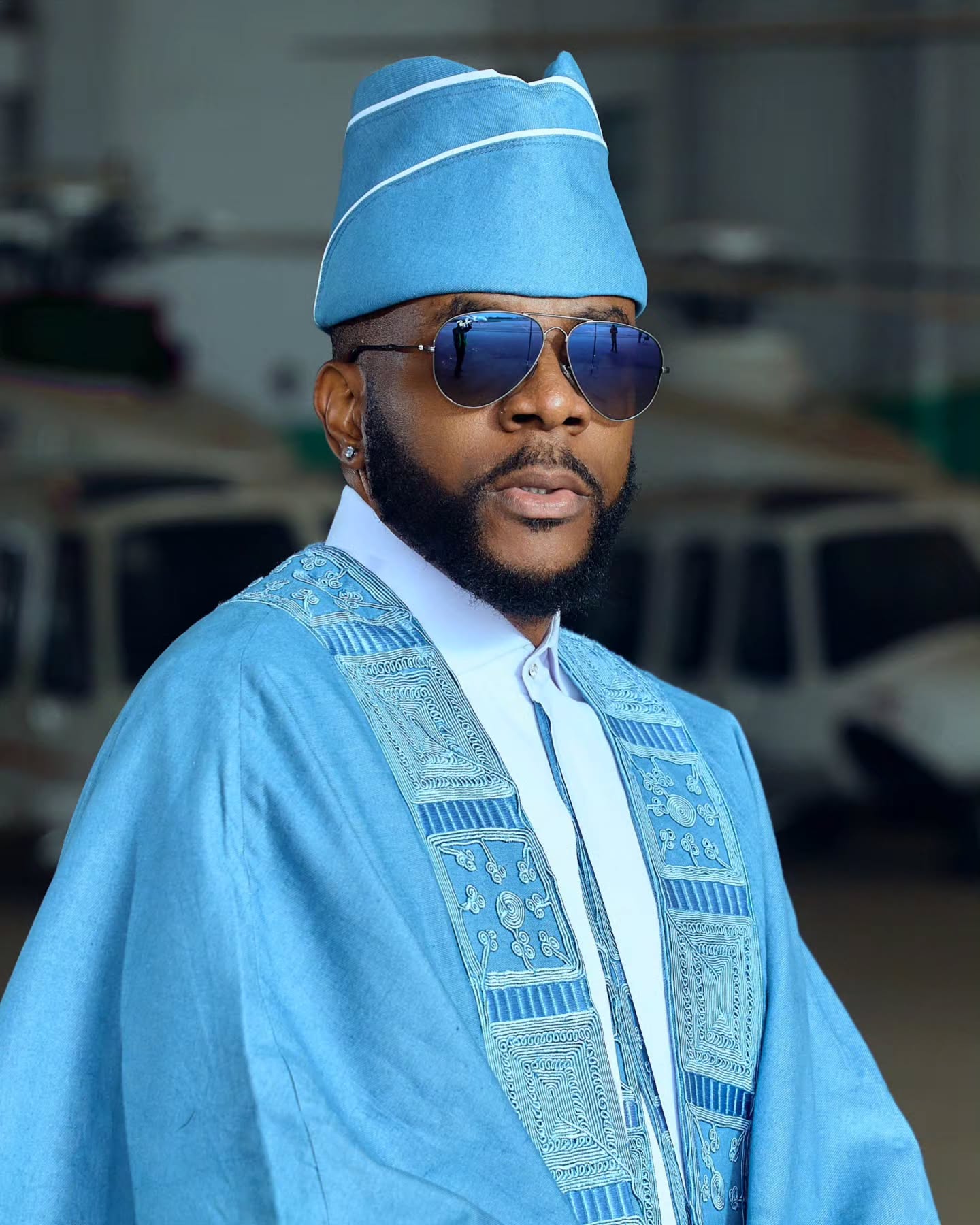Ebuka Obi-Uchendu wearing a matching sky-blue denim Fila cap, blue aviator sunglasses, and an embroidered Agbada collar by Deji and Kola.