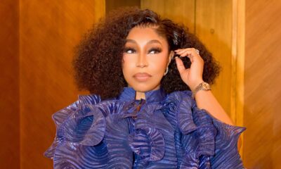 Detailed view of Rita Dominic wearing a royal blue metallic pleated ruffle blouse with a colourful tassel clutch bag at her birthday celebration.