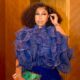 Detailed view of Rita Dominic wearing a royal blue metallic pleated ruffle blouse with a colourful tassel clutch bag at her birthday celebration.