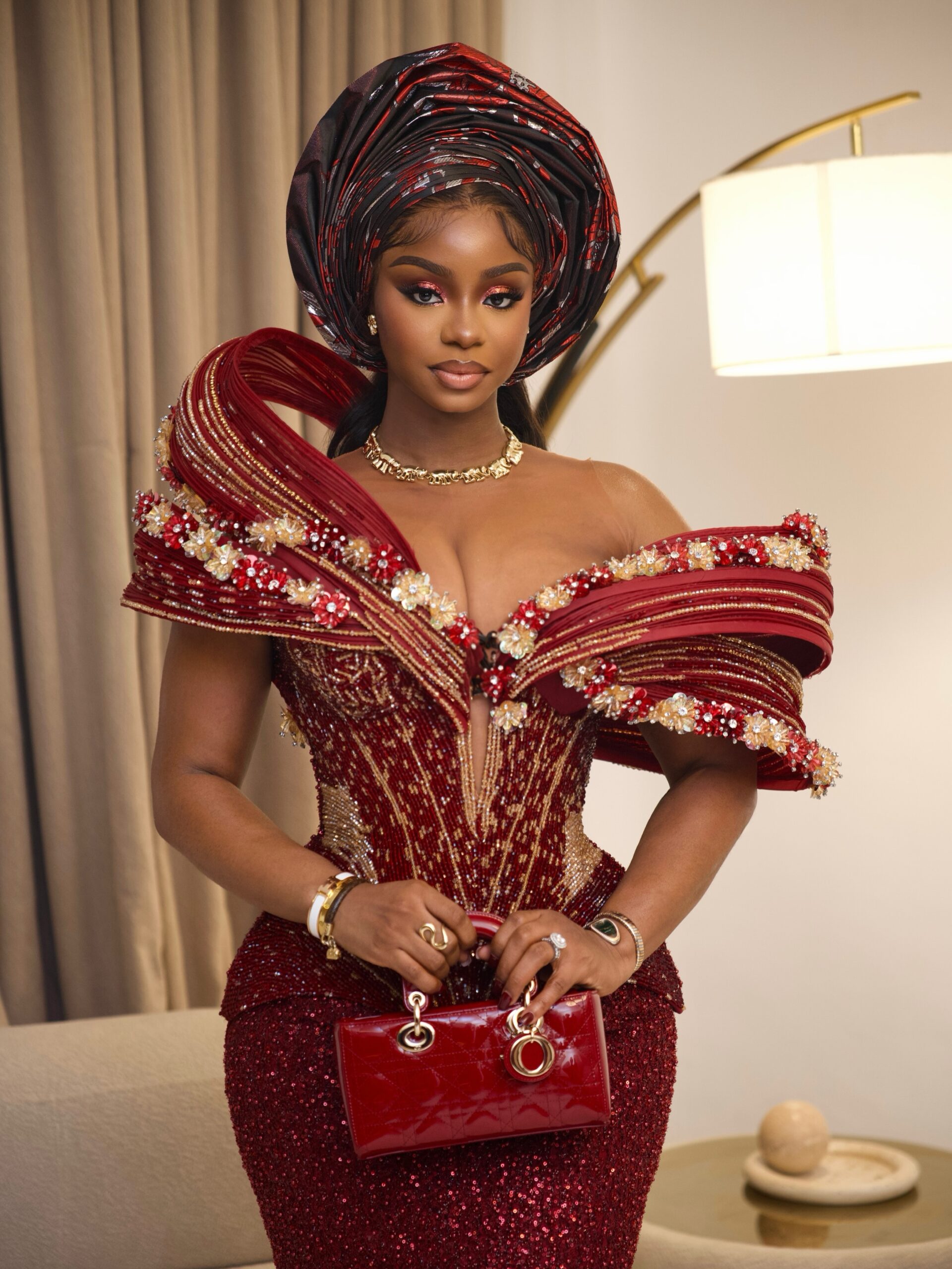 Priscilla Ojo wearing a beaded burgundy corset gown by Lasosa By Pam Pam with red Lady Dior handbag.