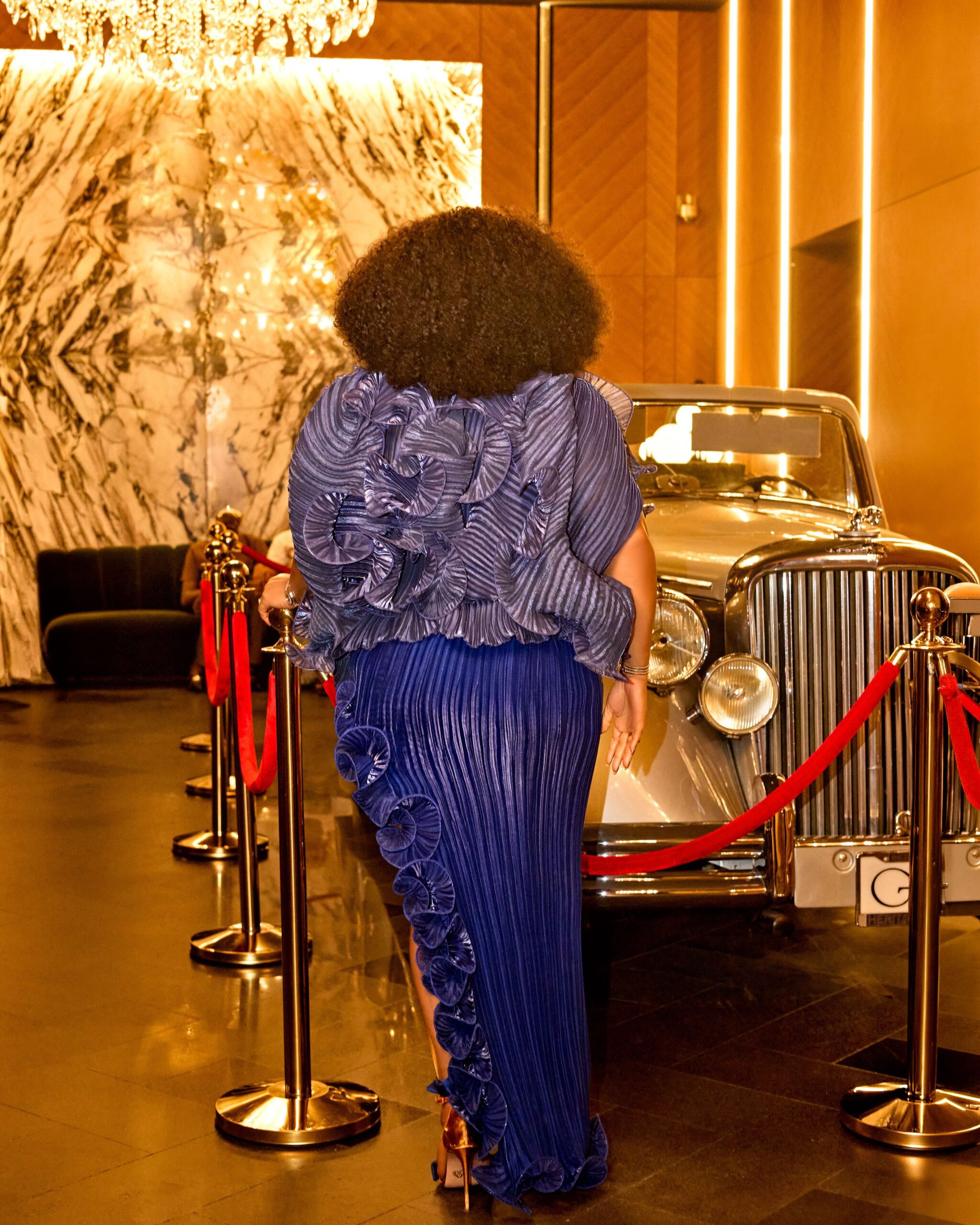 Rear view of Rita Dominic’s royal blue pleated velvet skirt showcasing the cascading ruffle border along the thigh-high side slit.