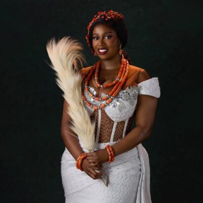 Temi Nkem wearing off-shoulder white lace attire paired with multi-layer coral necklaces and coral hair accessories.