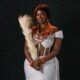 Temi Nkem wearing off-shoulder white lace attire paired with multi-layer coral necklaces and coral hair accessories.