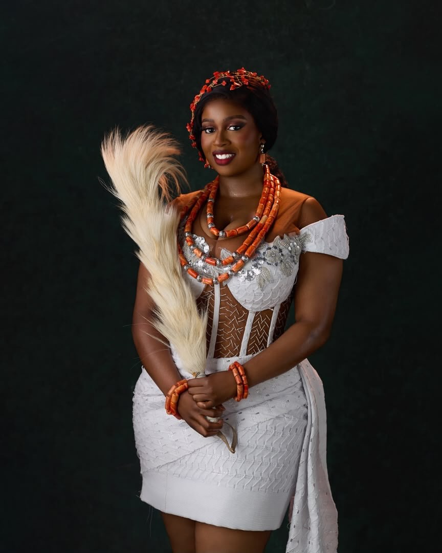 Temi Nkem wearing off-shoulder white lace attire paired with multi-layer coral necklaces and coral hair accessories.