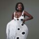 Close-up portrait of Nana Akua Addo wearing a white Hanifa knit dress with keyhole cut-out, oversized black polka dots, and holding a matching white fringe clutch.