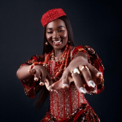 Big Brother Naija Season 11 housemate Goddessa smiling in a red beaded corset dress with traditional coral beads and a crown.