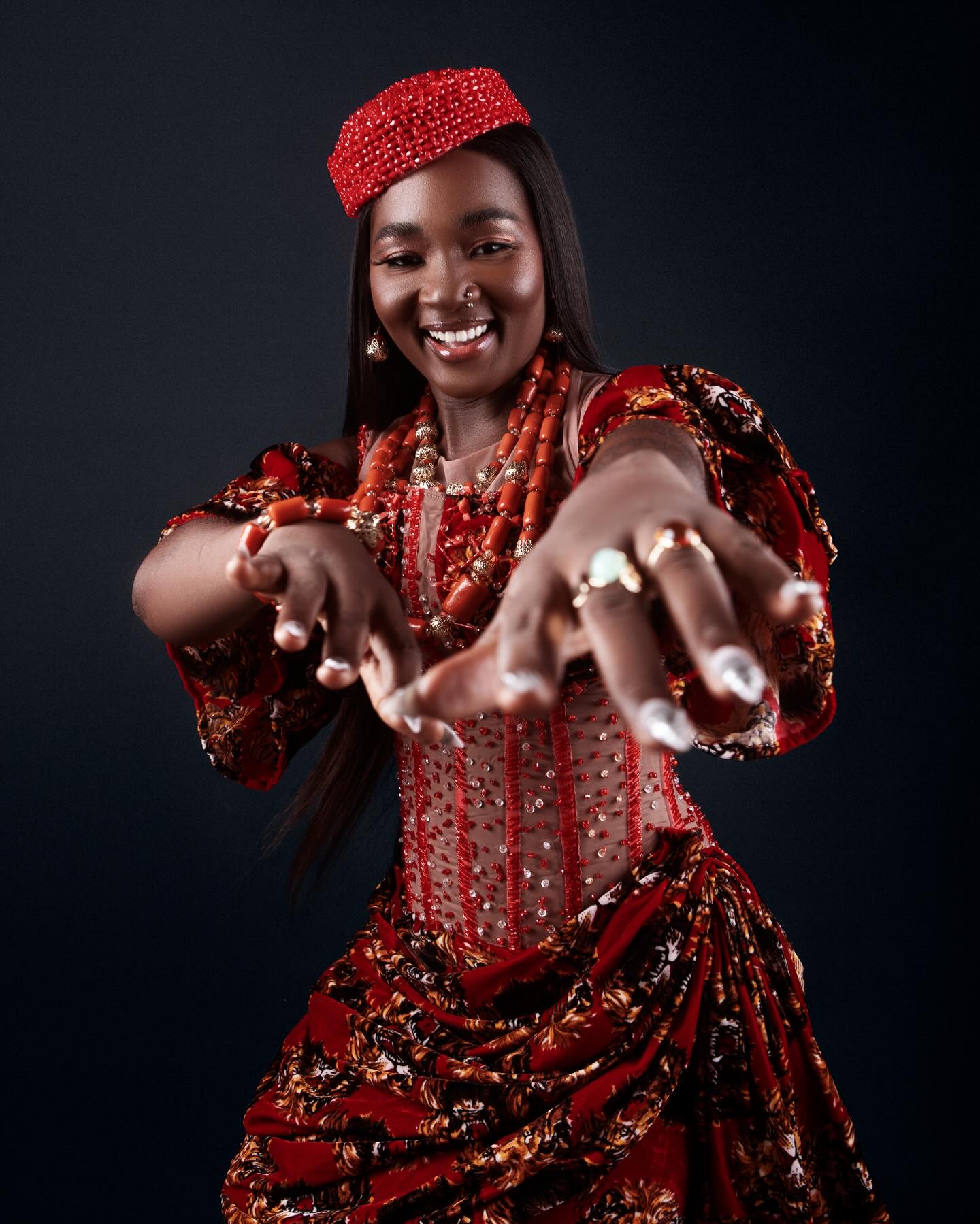 Big Brother Naija Season 11 housemate Goddessa smiling in a red beaded corset dress with traditional coral beads and a crown.