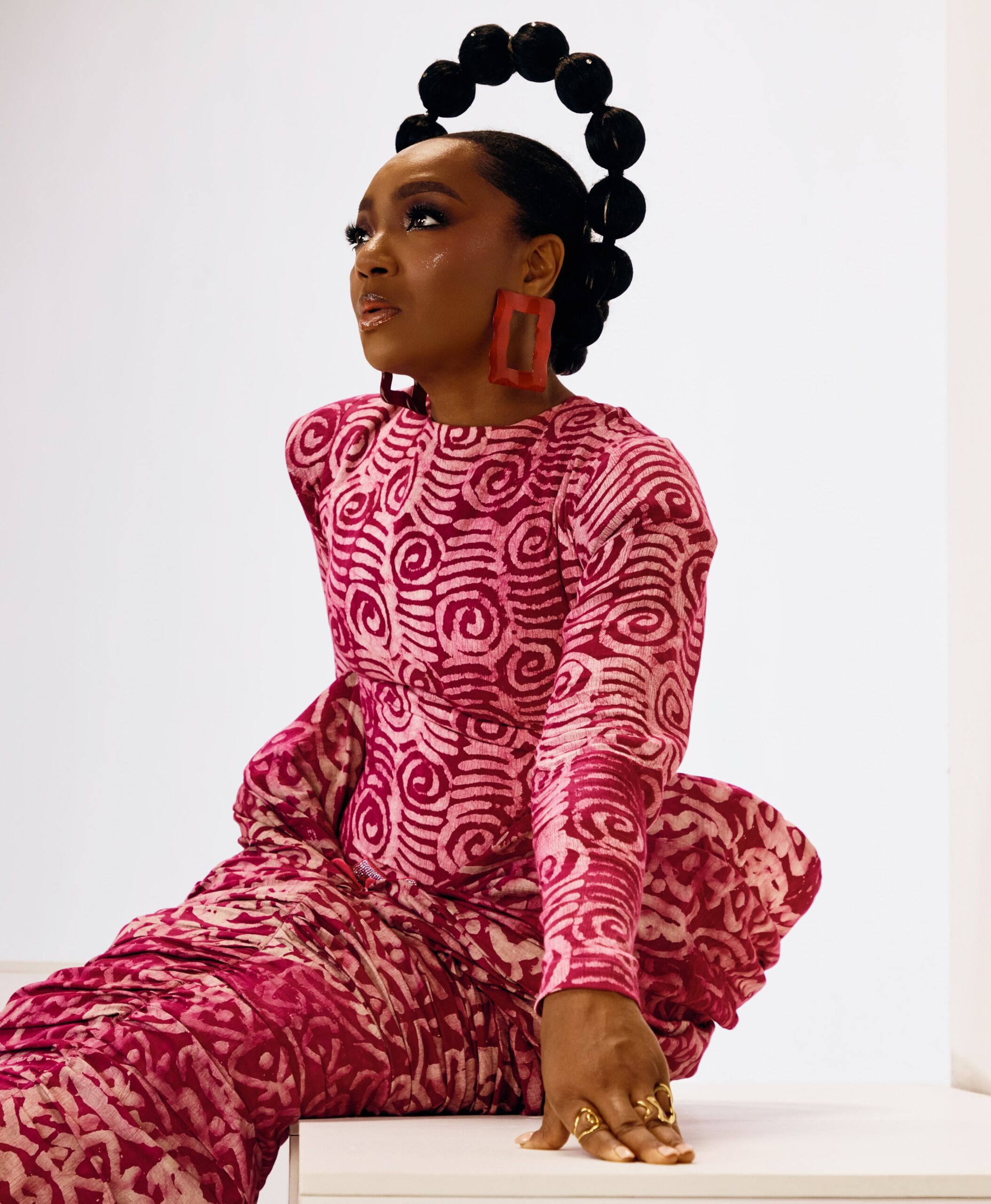 Chioma Akpotha wearing a pink patterned traditional outfit with a circular bubble hairstyle.