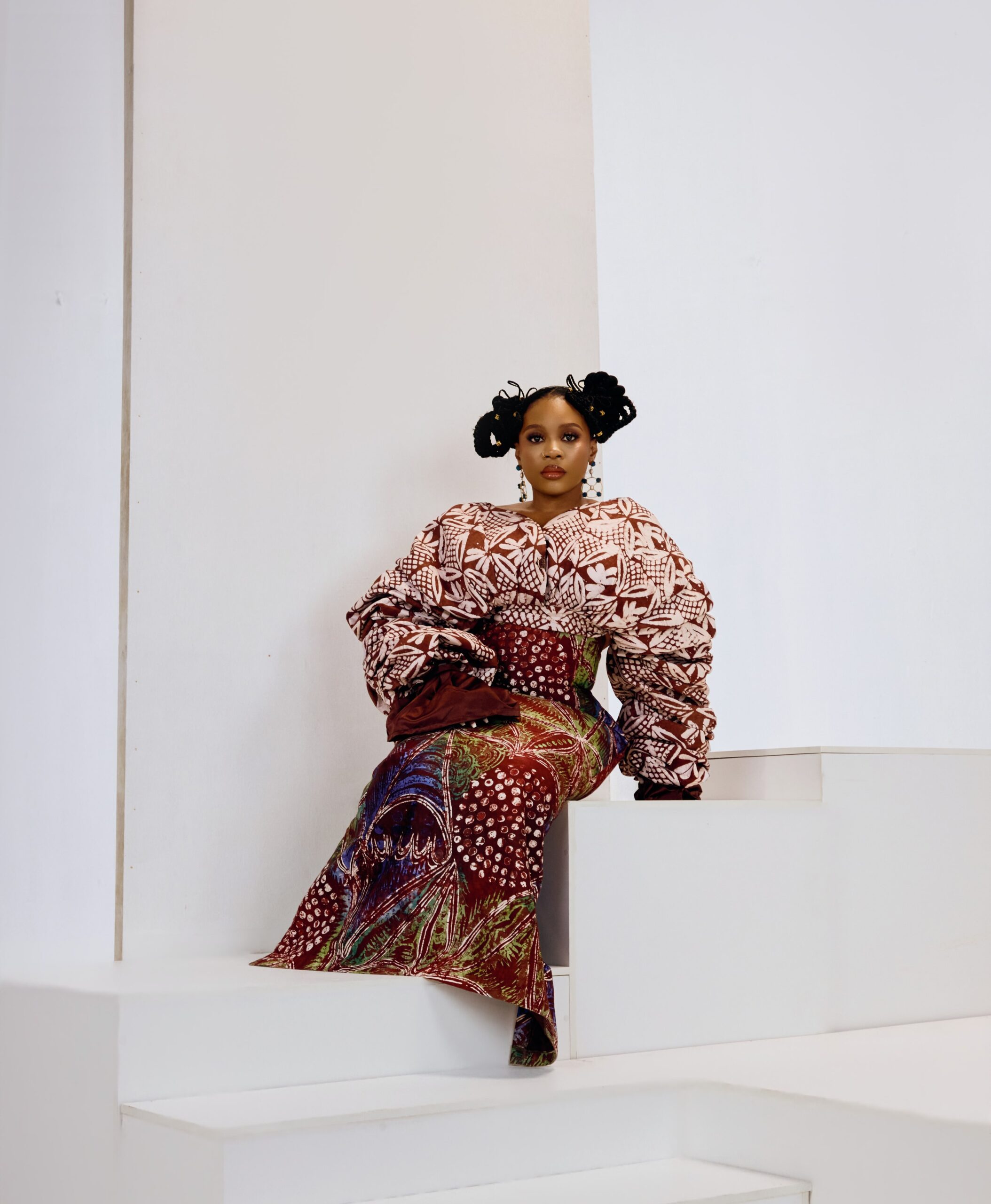 Wumi Toriola sitting in a patterned puff-sleeve top and traditional skirt with a double-bun hairstyle.