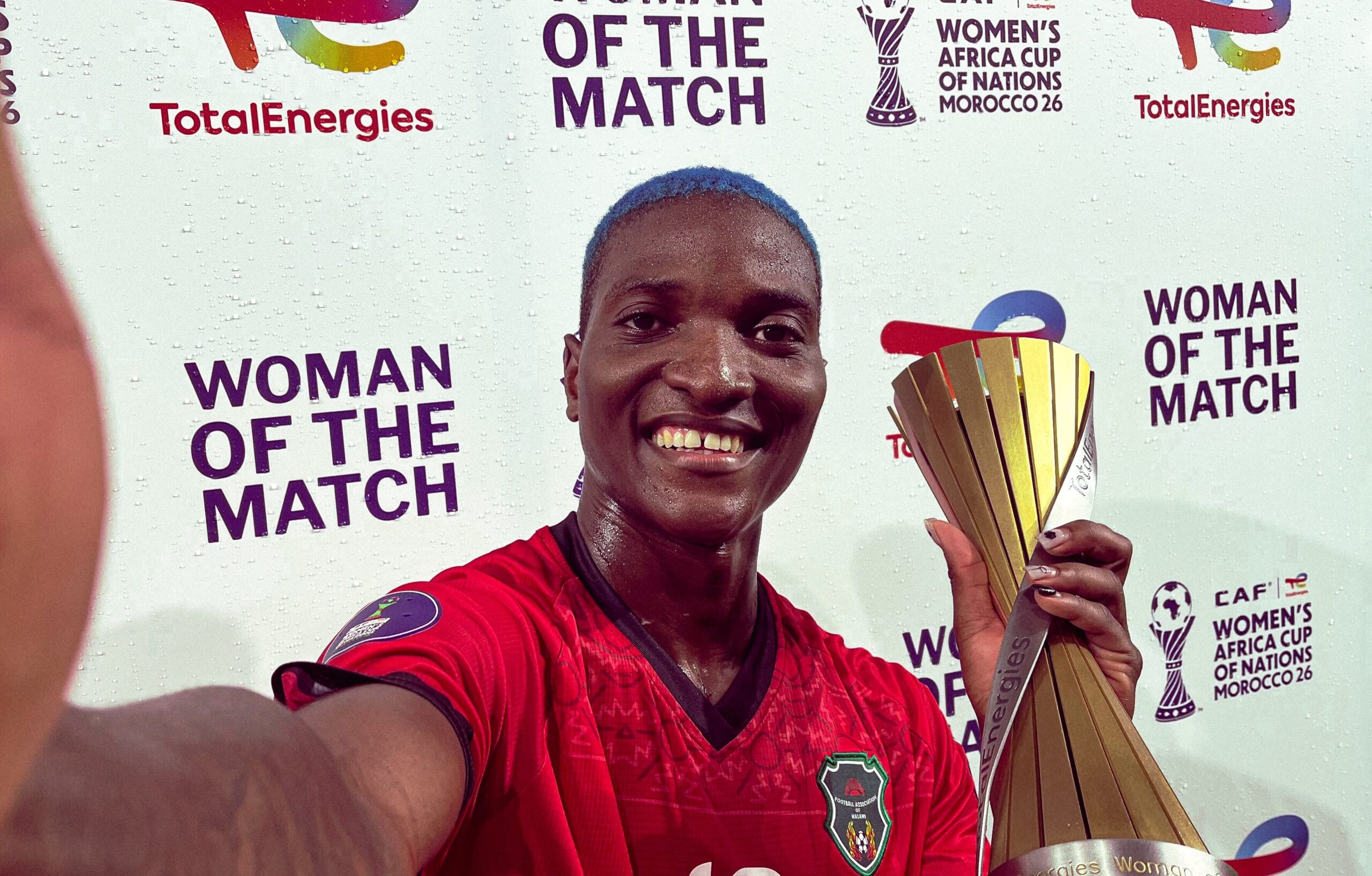 Selfie of Temwa Chawinga with blue hair holding her WAFCON Woman of the Match trophy after a Malawi victory.