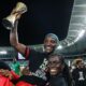 Tabitha Chawinga in locs carrying her sister Temwa Chawinga, who holds a trophy aloft wearing a FIFA Women's World Cup Qualified shirt.