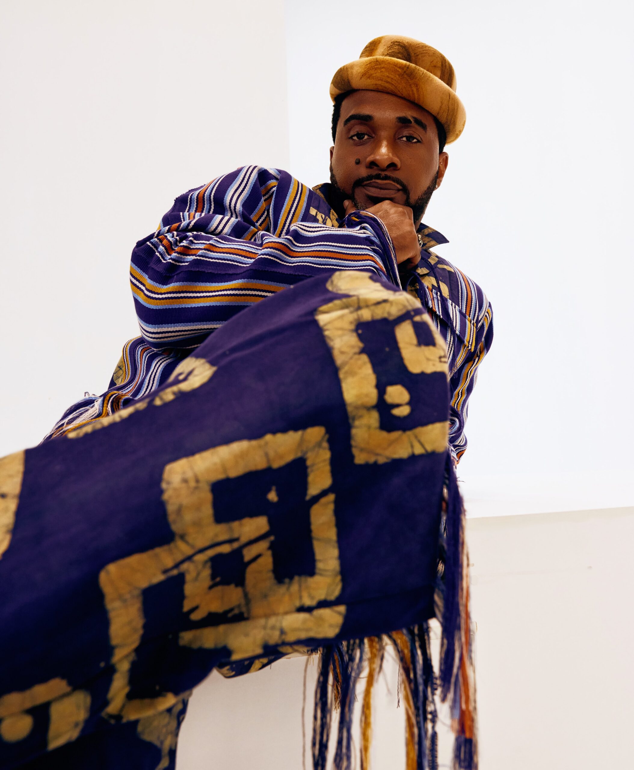 Uzor Arukwe posing in a blue striped traditional jacket and patterned trousers with a tan brimmed hat.