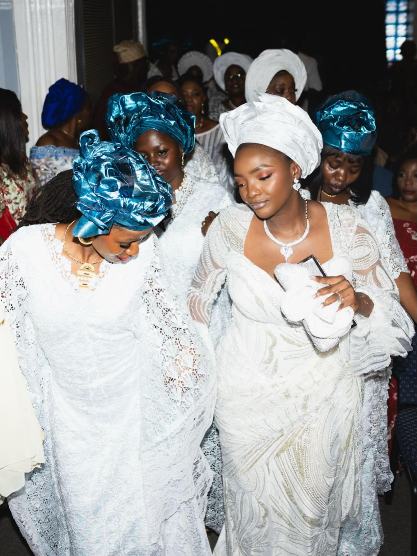 Simi walking alongside family members wearing matching white and teal headgears during a church service.
