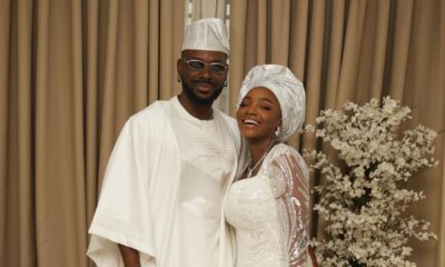 Simi and Adekunle Gold posing together in matching white traditional Yoruba outfits for their son Adeifemi's dedication.